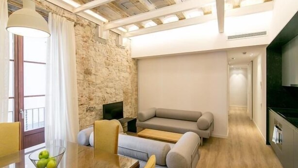 Un salon moderne avec un mur en pierre, un canapé, un téléviseur et un coin repas comprenant une table et des chaises.