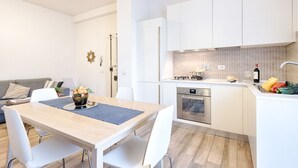 Een moderne keuken met witte kastjes, een eethoek met een tafel en stoelen, en een klein eiland met een spoelbak en aanrecht.