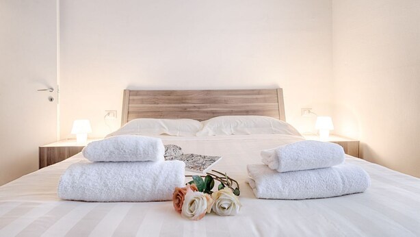 Een net opgemaakt bed met witte lakens, twee bedlampjes en een houten hoofdbord.