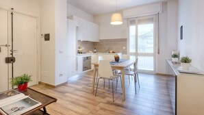 Een moderne keuken met witte kasten, een eethoek met een tafel en stoelen, en een groot raam met uitzicht.