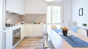 Een moderne keuken met witte kasten, een houten eettafel en een schaal met fruit.