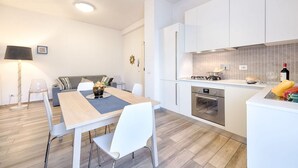 Een moderne keuken met witte kasten, een inbouwoven en een eethoek met een tafel en stoelen.