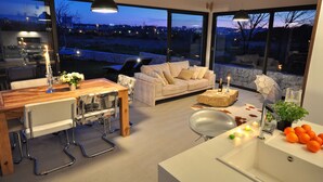 A modern living room with a large window, a dining area with a wooden table, and a kitchen area with a sink and countertop. - Luxury Villa In Split, Few Minutes To Center, Beaches, Shopping, Sport Courts (Split)