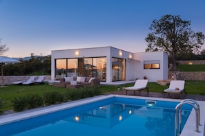 Una casa moderna con piscina, mobiliario exterior y un muro de piedra.