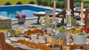 A breakfast setup with croissants, cheese, and fruit by a poolside with a view of the pool and greenery. - Luxury Villa In Split, Few Minutes To Center, Beaches, Shopping, Sport Courts (Split)