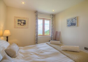 A bedroom with two beds, a window with curtains, a lamp, and two framed pictures on the walls.