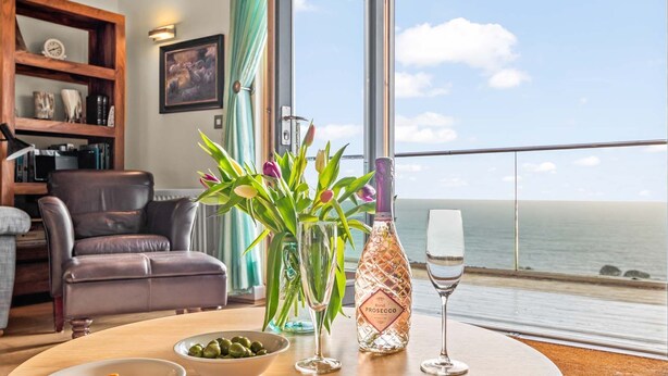 Una habitación con vista al mar, una mesa redonda con una botella de Prosecco rosado, una copa de vino y cuencos de aperitivos.