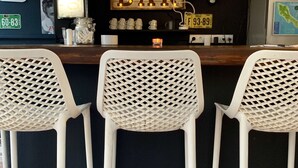 A bar area with three white plastic chairs, a sign reading "BAR", and various decorations including a clock and a map.