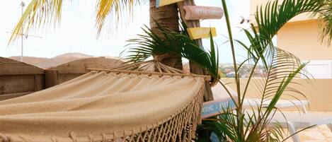 A hammock tied to a palm tree, a wooden signpost with directional signs, and a view of a building in the background.