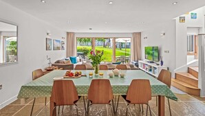 A dining area with a large table, chairs, and a view of a garden.