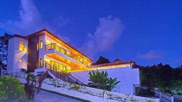 A modern two-story house with a white exterior, a balcony on the upper floor, and a staircase leading to the entrance.