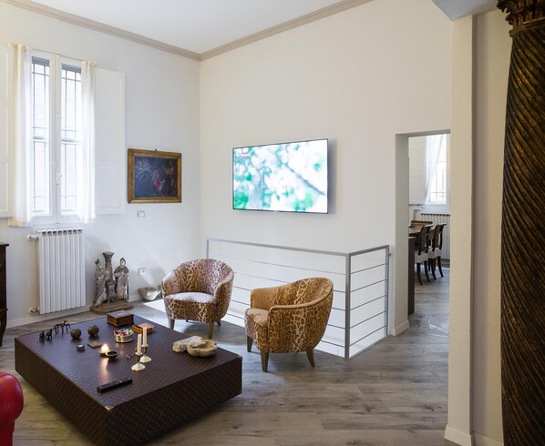 A living room with a large flat-screen TV, two leopard print armchairs, a coffee table with decorative items, and a painting on the wall.