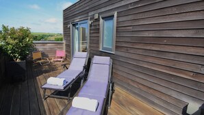 Een houten terras met twee ligbedden en een kleine tafel, met uitzicht op een prachtig landschap.