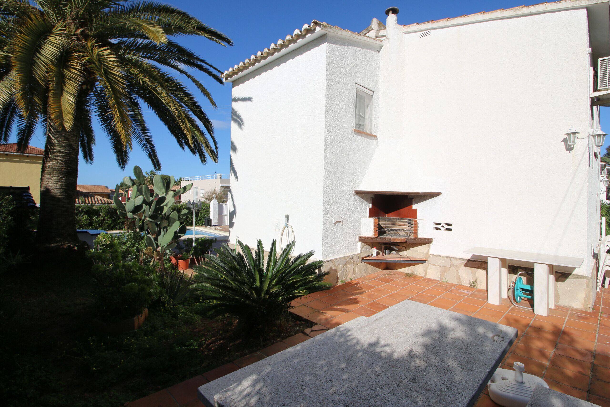 A white building with a tiled patio, a cactus, and a palm tree.