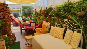 A cozy room with a hammock, a bed with patterned pillows, and lush green plants. - Family house with pool by the beach (Atouguia da Baleia)