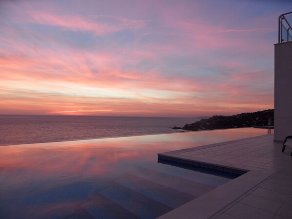 Une piscine à débordement offrant une vue sur l’océan au coucher du soleil.