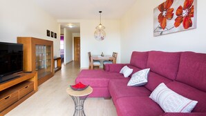 A modern living room with a sectional sofa, a flat-screen TV, a dining area with a table and chairs, and a wall-mounted clock. - Adeje with pool, sea view and WIFI gratis (Adeje)