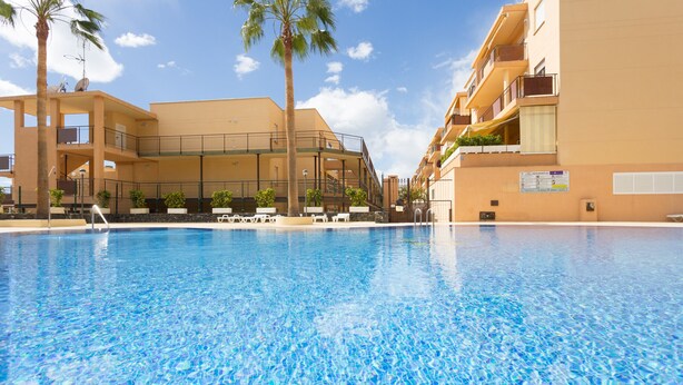 A swimming pool with clear blue water, surrounded by multi-story buildings with balconies and outdoor seating areas. - Adeje with pool, sea view and WIFI gratis (Adeje)