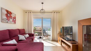A modern living room with a red sofa, a flat-screen TV on a wooden stand, and a balcony with a view of the city. - Adeje with pool, sea view and WIFI gratis (Adeje)