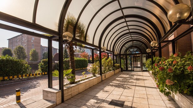 Un paseo techado con suelo de baldosas, paneles de vidrio y macetas con plantas.