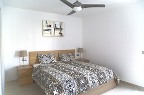 A bedroom with a bed, two bedside tables, a ceiling fan, and a wall-mounted painting.