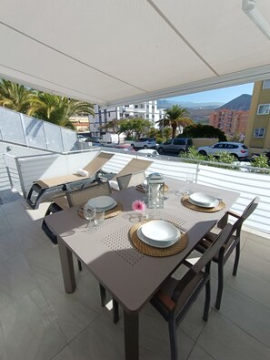 An outdoor dining area with a table set for four, surrounded by chairs, on a terrace with a view of buildings and parked cars. - Idaira III new spacious apartment with private garage and beach walking distance (Los Cristianos)