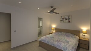 A bedroom with a bed, two bedside tables with lamps, a ceiling fan, and a bathroom visible through an open door. - Idaira III new spacious apartment with private garage and beach walking distance (Los Cristianos)