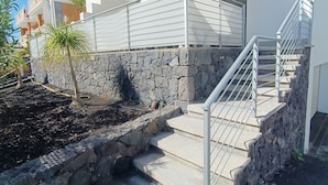 A modern building with a stone retaining wall, a covered staircase, and a clear sky. - Idaira III new spacious apartment with private garage and beach walking distance (Los Cristianos)
