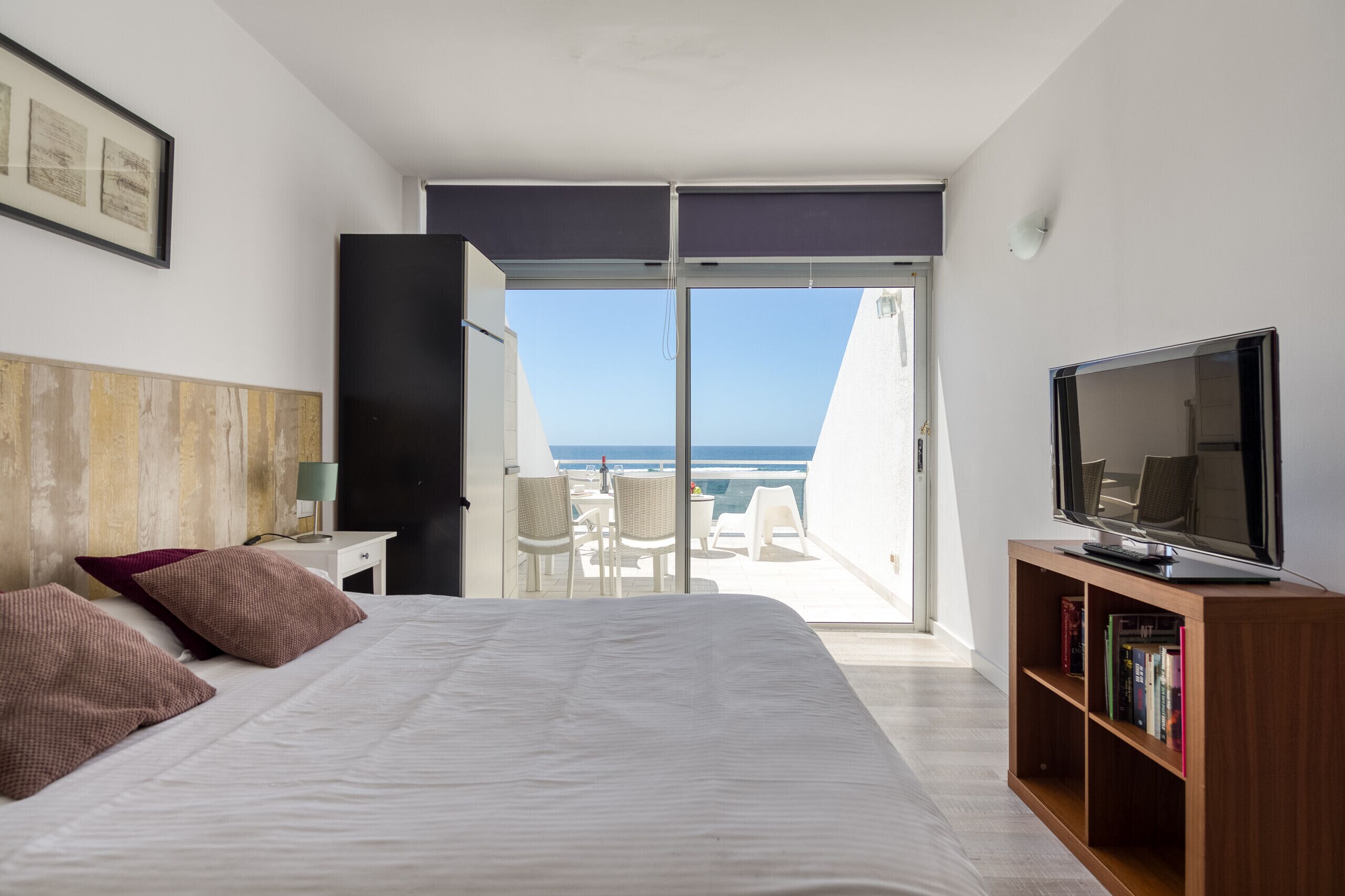 A bedroom with a large bed, a television, and a view of the ocean.