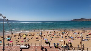 Uma praia com pessoas se banhando e tomando sol, uma torre salva-vidas e um céu azul límpido.