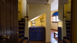 Ein Flur mit Holzboden und einer Wendeltreppe, ein blaues Schranks mit Lampe und Blumen, sowie ein Fenster mit blauer Glasverkleidung.