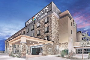 Ein Hotel mit Stein-Fassade, einem überdachten Eingang und einem Schild mit der Aufschrift 'Four Points by Sheraton'.