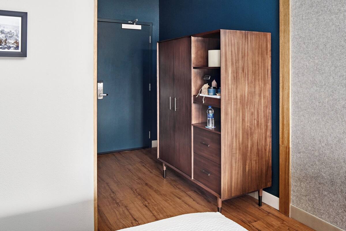 Quarto com guarda-roupa de madeira, uma cama e uma porta que dá para outro cômodo.