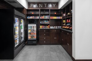 Uma despensa com prateleiras repletas de lanches e bebidas, uma geladeira e um micro-ondas.