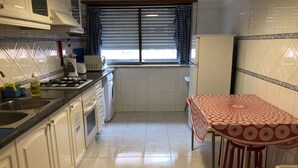 A kitchen with white cabinets, a gas stove, a washing machine, a refrigerator, and a table with a red and white tablecloth. - FAMILY APARTMENT LISBON - TAGUSPARK (São Marcos)