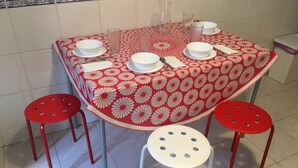 A dining table set with white plates, bowls, and cutlery, surrounded by four red stools. - FAMILY APARTMENT LISBON - TAGUSPARK (São Marcos)