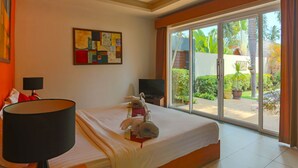 Ein Hotelzimmer mit Bett, Deckenventilator, Fernseher und Blick auf den Garten durch die Schiebetür.