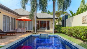 Piscina con baldosas azules, rodeada por un patio con mobiliario exterior y una palmera.