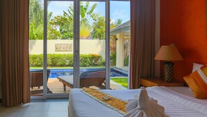 Habitación de hotel con cama, mesita de noche, lámpara y vista a una piscina y vegetación.