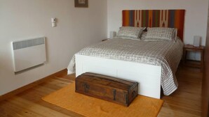 Een slaapkamer met een bed, een dressoir, een radiator en een kleurrijk gordijn.