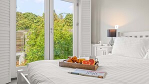 Ein Schlafzimmer mit großem Fenster, Nachttisch mit Lampe und Tablett mit Croissants und Orangen auf dem Bett.