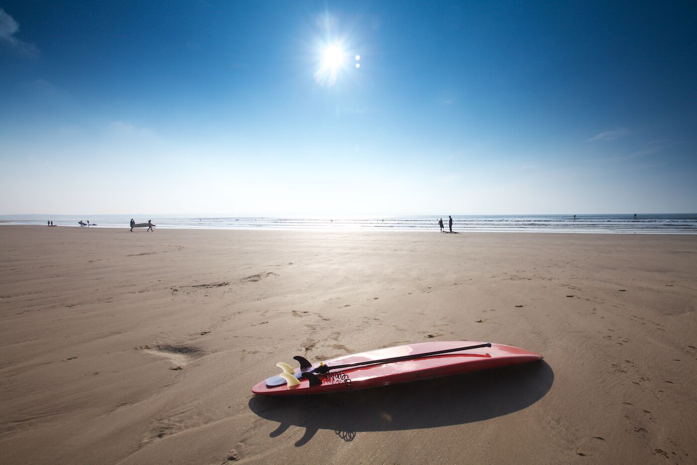 Ampia spiaggia sabbiosa con una tavola da surf rossa in primo piano e cielo azzurro limpido.