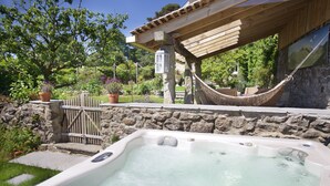 Un jacuzzi con un muro de piedra de fondo, una hamaca y una pérgola de madera.