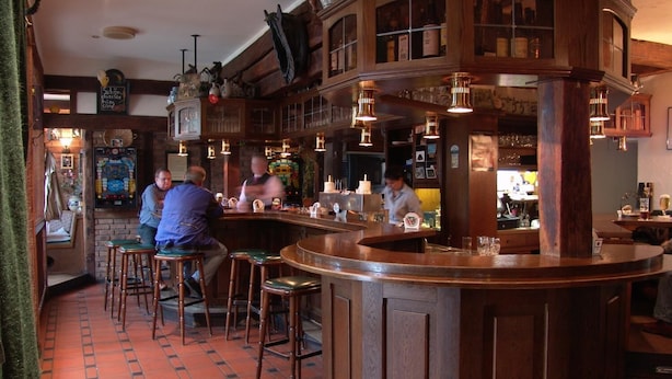 A bar area with wooden bar counters, stools, and a tiled floor.
