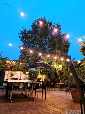 An outdoor patio area with tables and chairs, string lights, and an umbrella. - Hotel Altes Gasthaus Düsterbeck (Emsdetten)