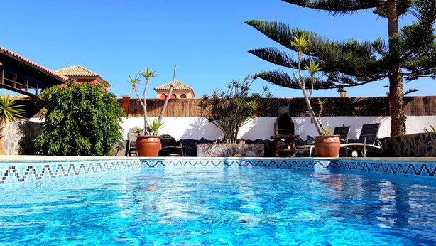 A clear blue pool with a tiled edge, surrounded by lounge chairs and potted plants. - Wonderful villa with a large private heated pool and stunning views to the dunes (Corralejo)