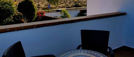 A balcony with two chairs and a table, overlooking a desert landscape with mountains in the distance.