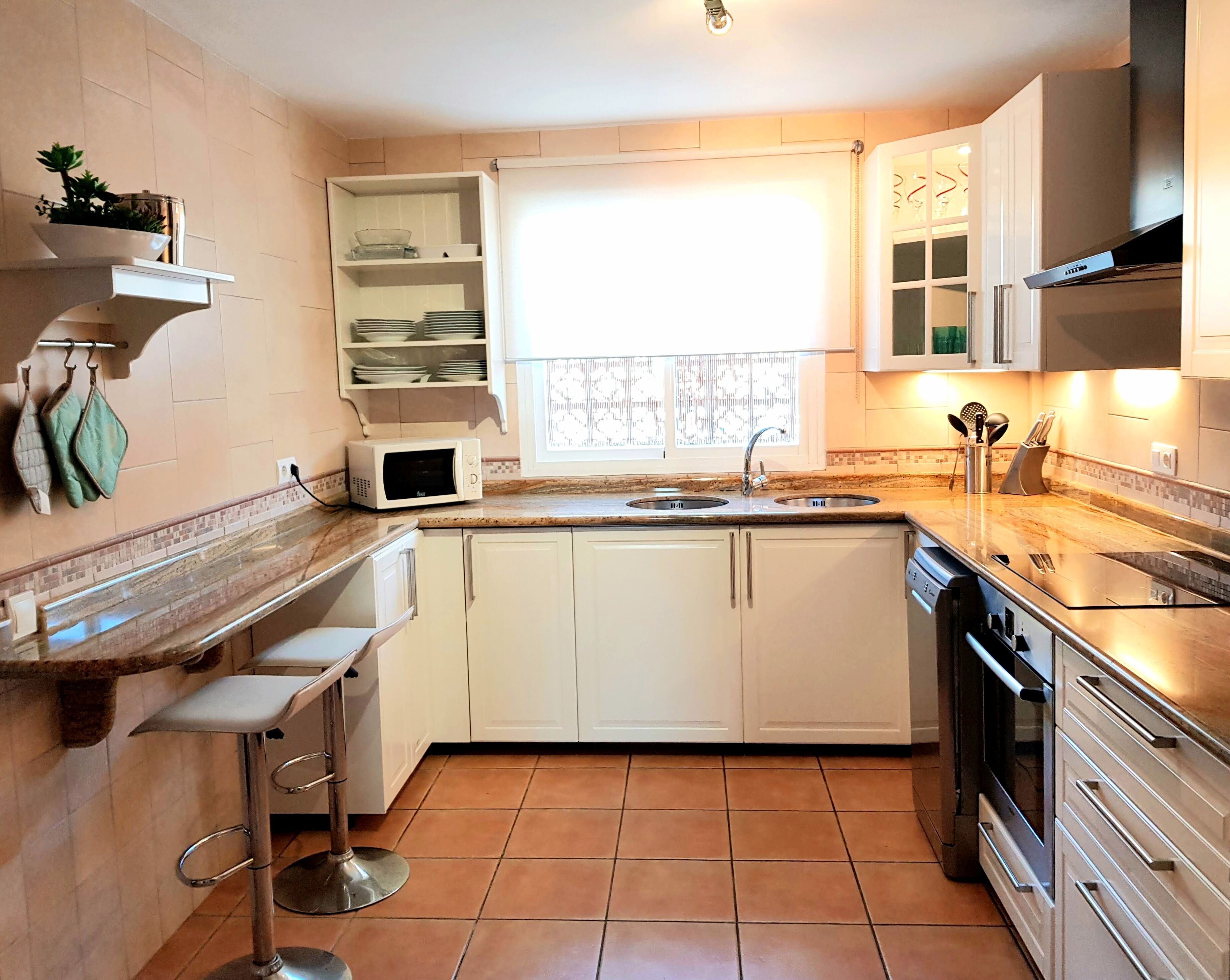 Une cuisine compacte avec des meubles blancs, un four à micro-ondes encastré, un évier et une cuisinière.