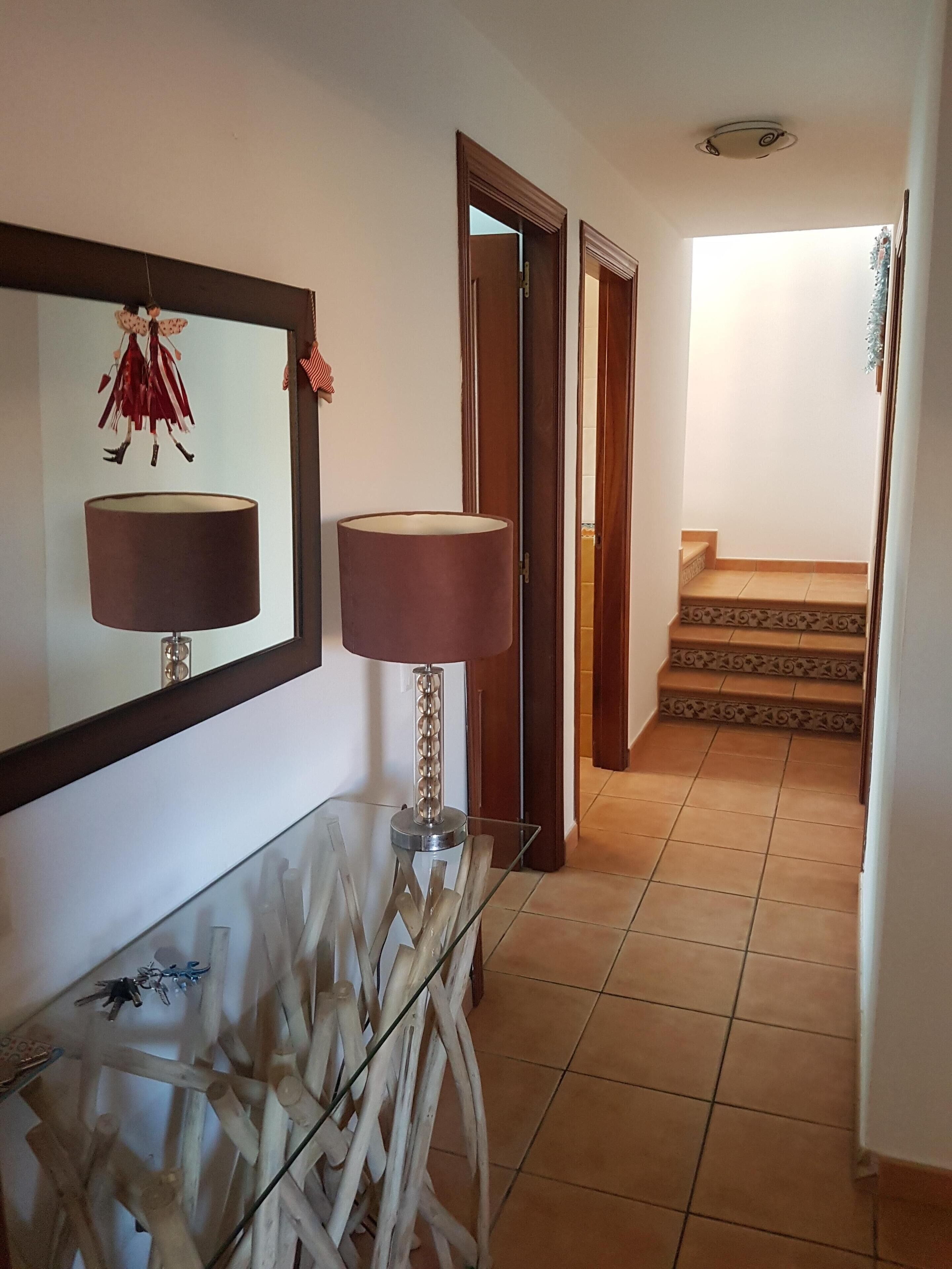 A hallway with a glass console table, two lamps, a mirror, and a staircase leading to another room.