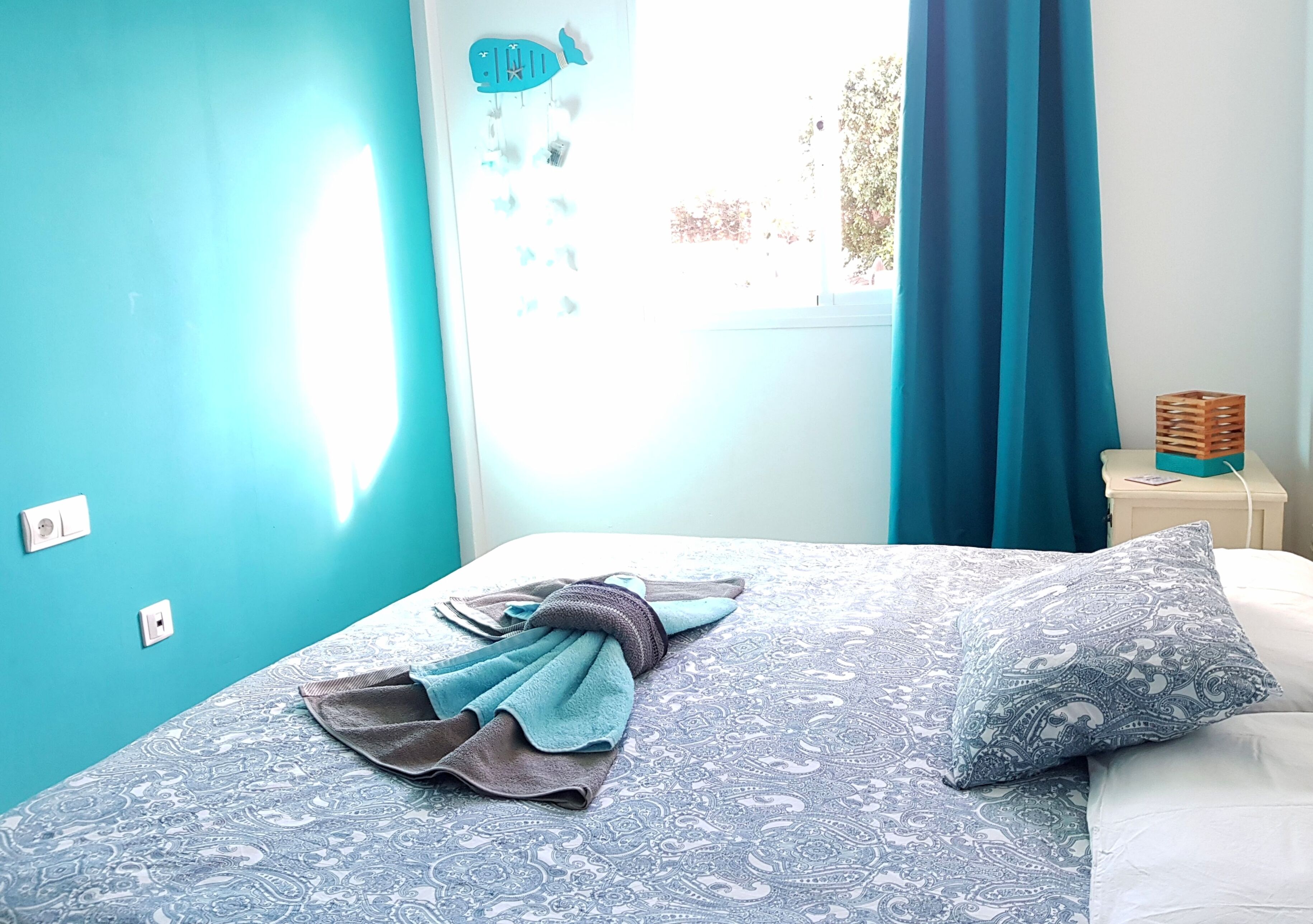Une chambre à coucher comprenant un lit, une table de chevet, une fenêtre avec des rideaux et un décor mural représentant des poissons.